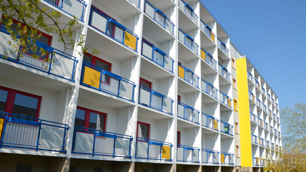 Wohnhaus am Doblinaweg mit blauen Balkongeländern und gelber Fassadenfläche unter blauem Himmel