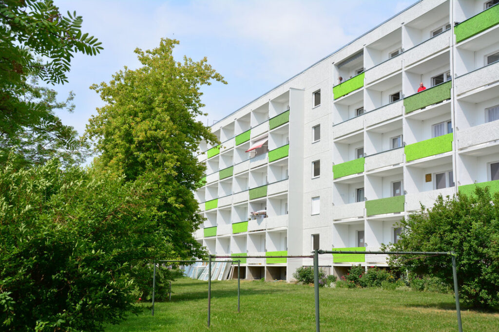 Wohnhaus „Sonnenterrassen“ mit hellgrünen Balkonen hinter Bäumen und Rasen