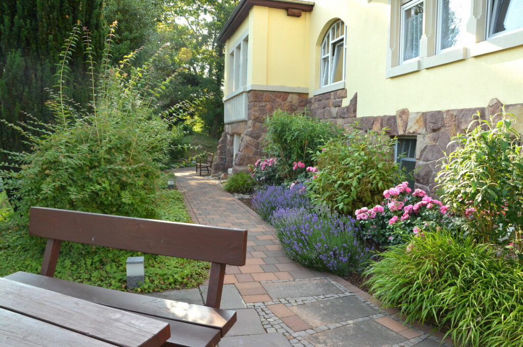 Gepflegter Garten mit Holzbank, Lavendel und blühenden Beeten vor dem Haus