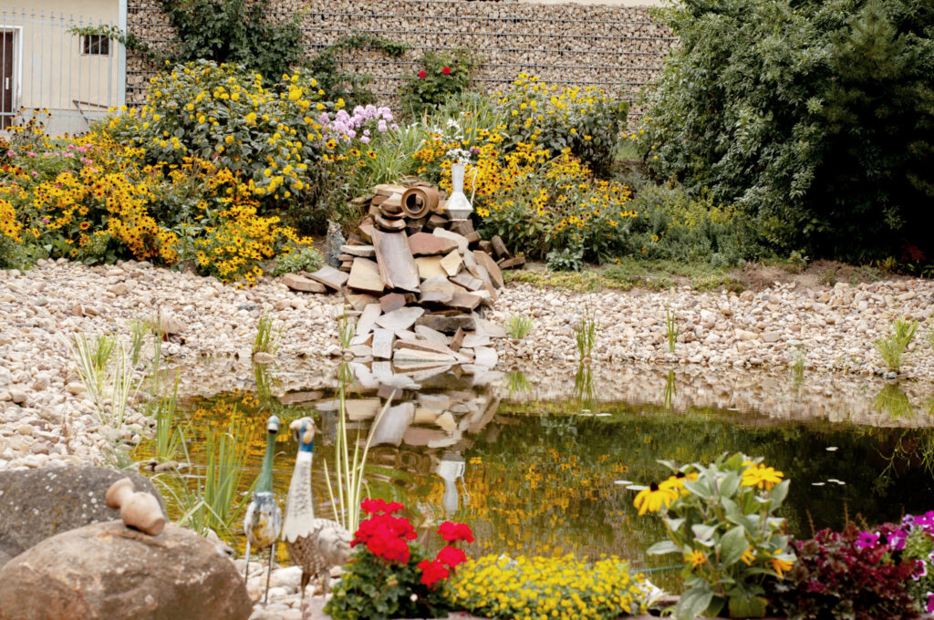 Steinteich mit kleinem Wasserlauf, umgeben von gelben und roten Blumen