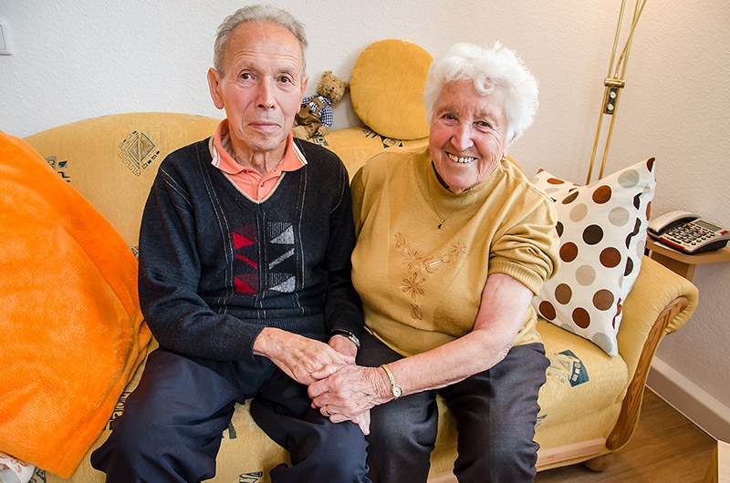 Älteres Ehepaar sitzt Hand in Hand auf dem Sofa in seiner Wohnung