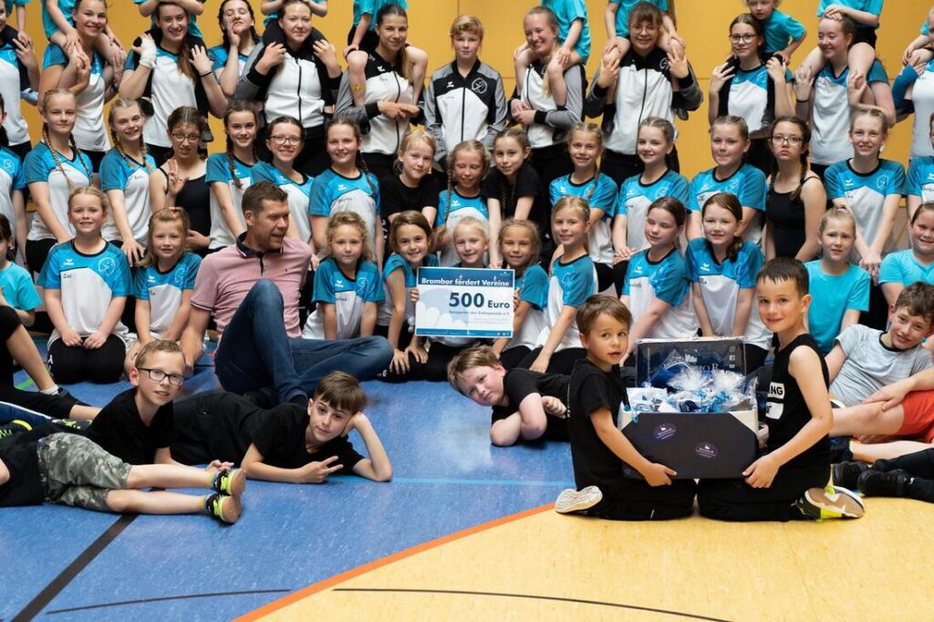 Große Tanzgruppe aus Kindern und Jugendlichen posiert in einer Turnhalle mit einem Spendenscheck über 500 Euro