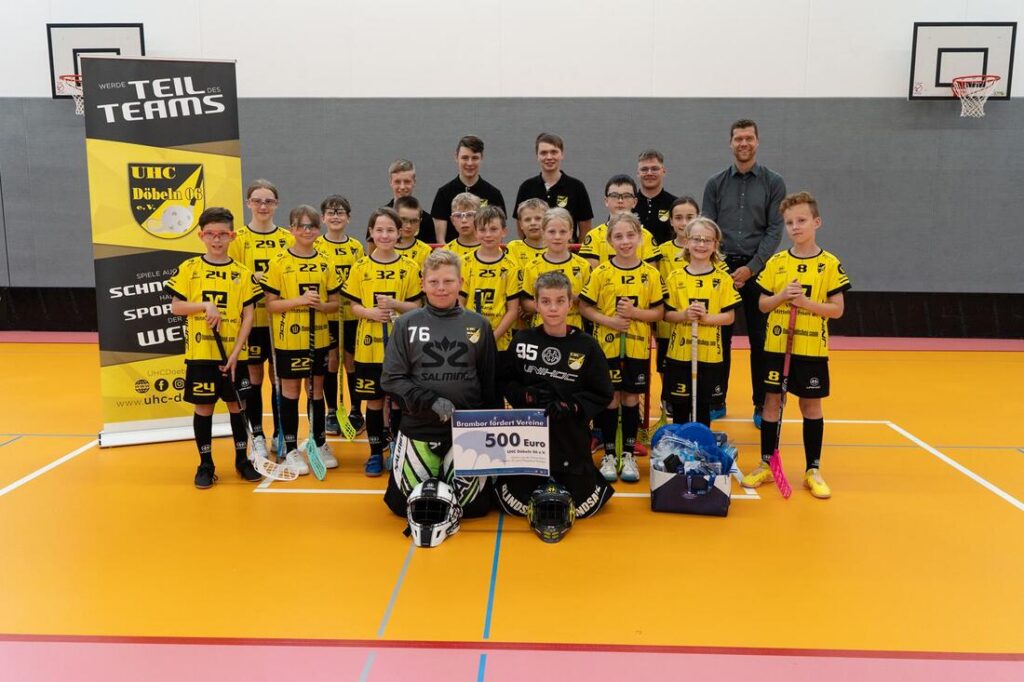 Junge Unihockey-Spielerinnen und -Spieler in gelben Trikots mit ihren Trainern in einer Turnhalle