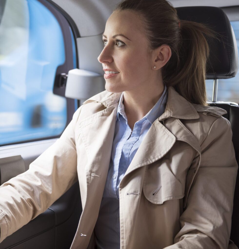 Lächelnde Fahrgästin schaut auf der Rückbank eines Taxis aus dem Fenster