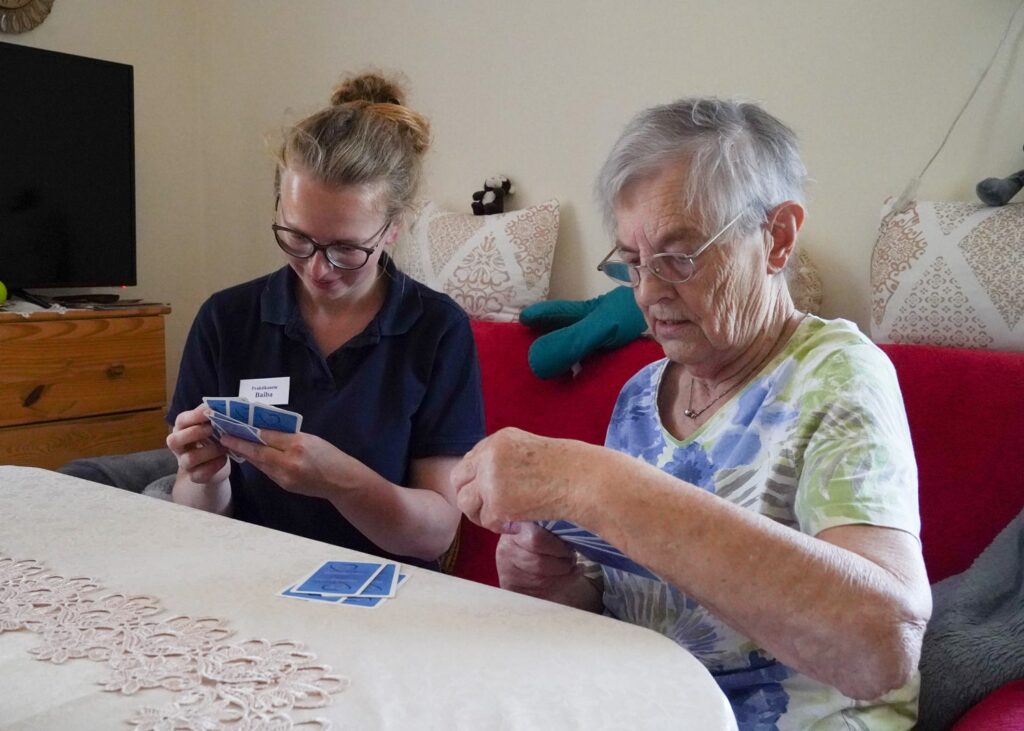Pflegerin und Seniorin spielen gemeinsam Karten im Wohnzimmer