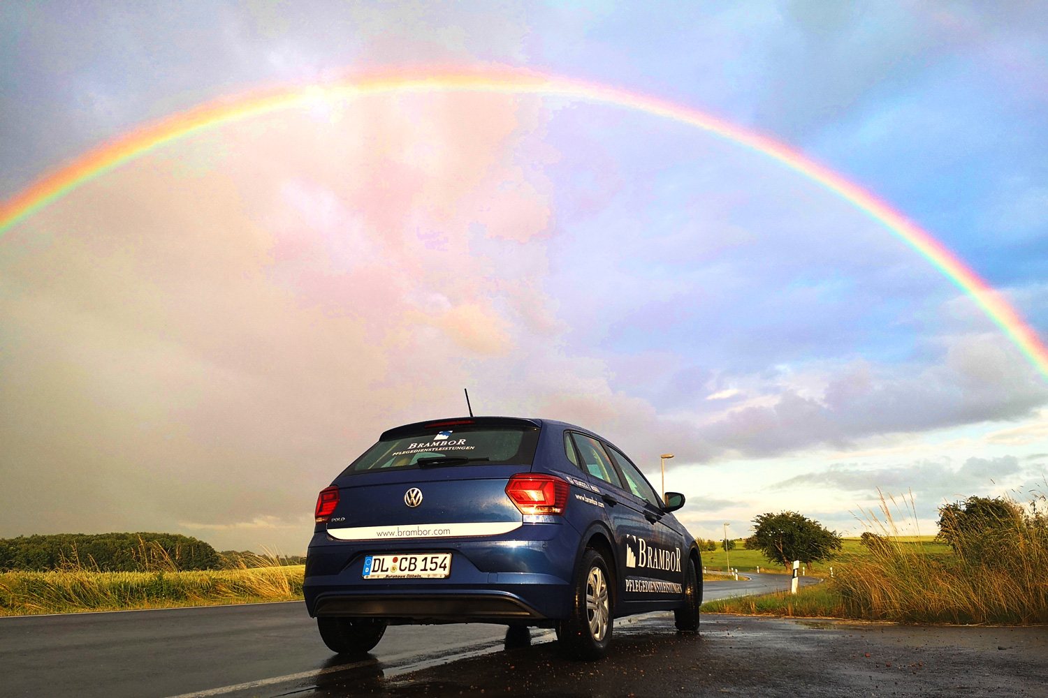 Blauer Brambor-Dienstwagen auf einer Landstraße unter einem Regenbogen