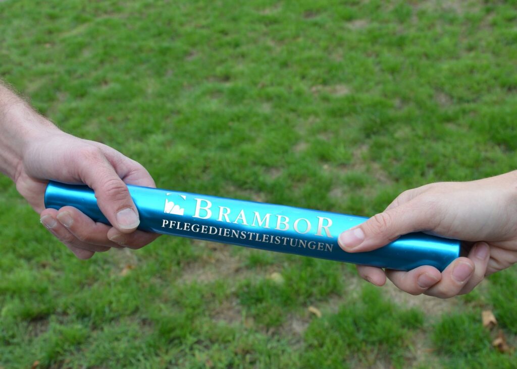Zwei Hände übergeben einen blauen Staffelstab mit Brambor-Logo