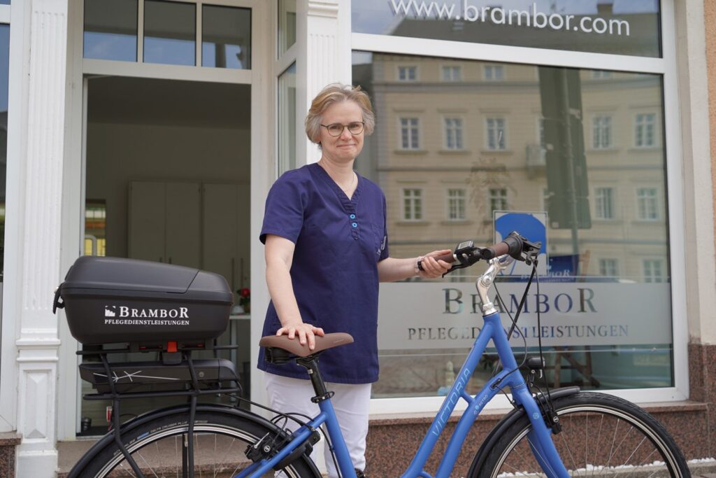 Pflegerin mit Brambor-E-Bike vor einer Brambor-Geschäftsstelle