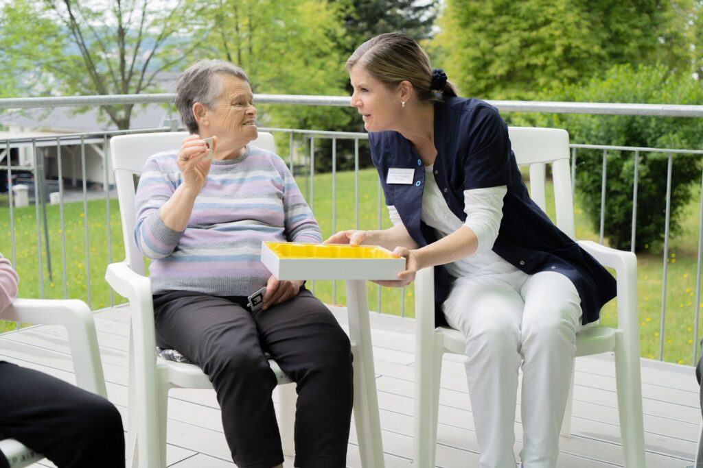 Pflegerin unterhält sich auf der Terrasse der Tagespflege mit einer Seniorin