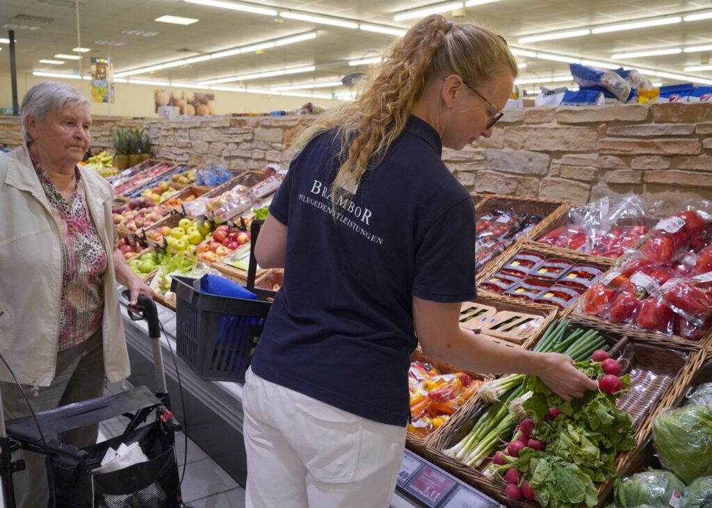 Junge Pflegekraft kauft mit einer Seniorin im Supermarkt Obst und Gemüse ein