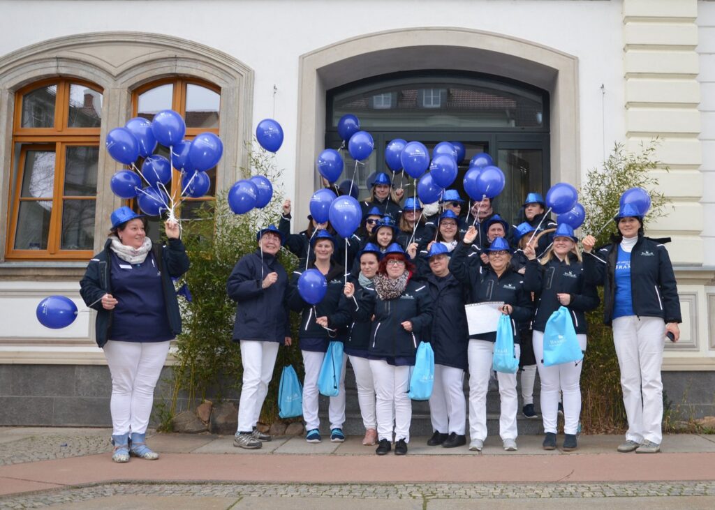 Großes Brambor-Team in blauer Dienstkleidung mit blauen Luftballons vor einem Gebäude