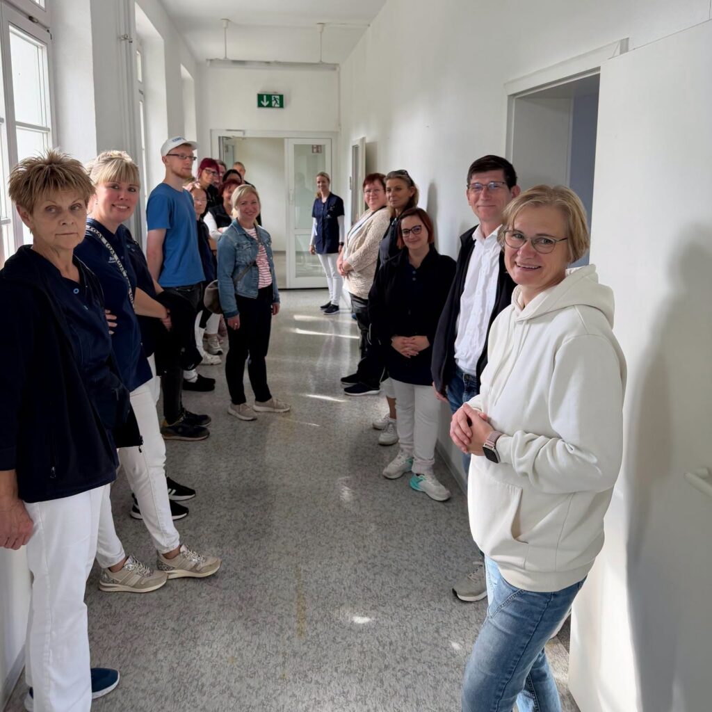 Mitarbeitende stehen im hellen Flur des Gebäudes und lächeln in die Kamera