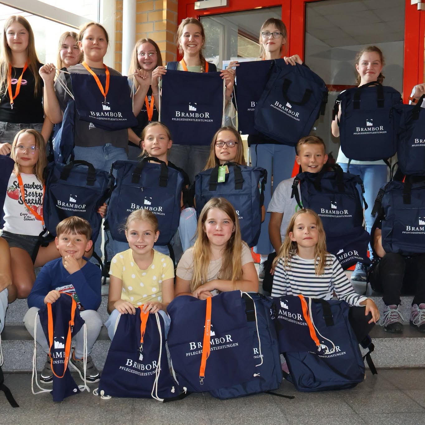 Eine große Gruppe Kinder der Roßweiner Spielleute sitzt und steht auf einer Treppe, alle halten Rucksäcke und Beutel mit dem Brambor-Logo