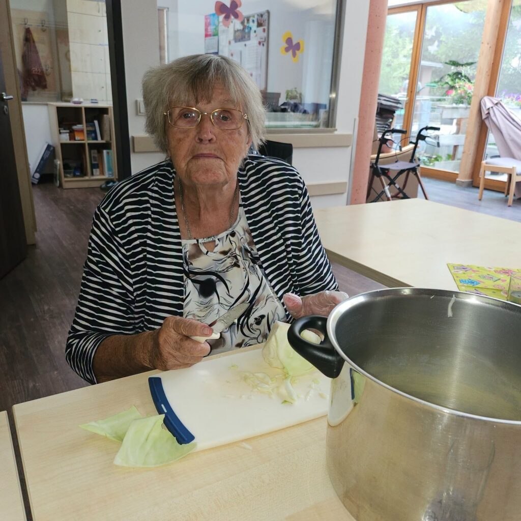 Eine Seniorin schneidet am Tisch Weißkohl, vor ihr steht ein großer Kochtopf