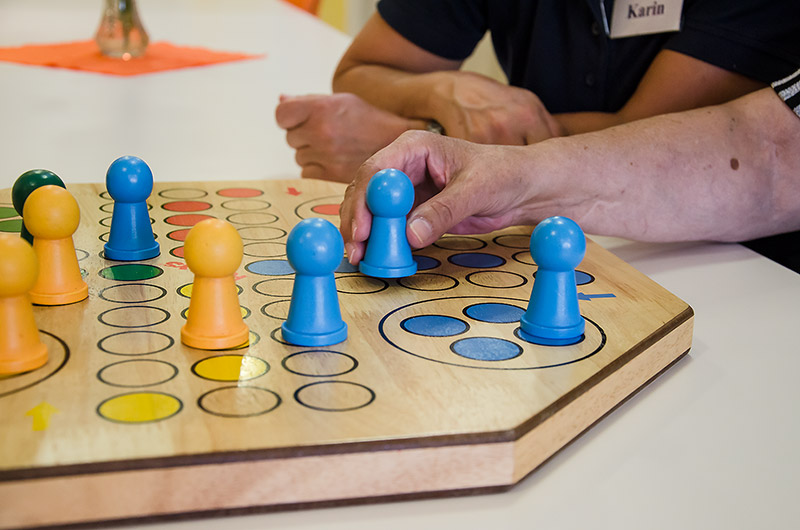 Hände setzen blaue Spielfiguren auf einem hölzernen Brettspiel