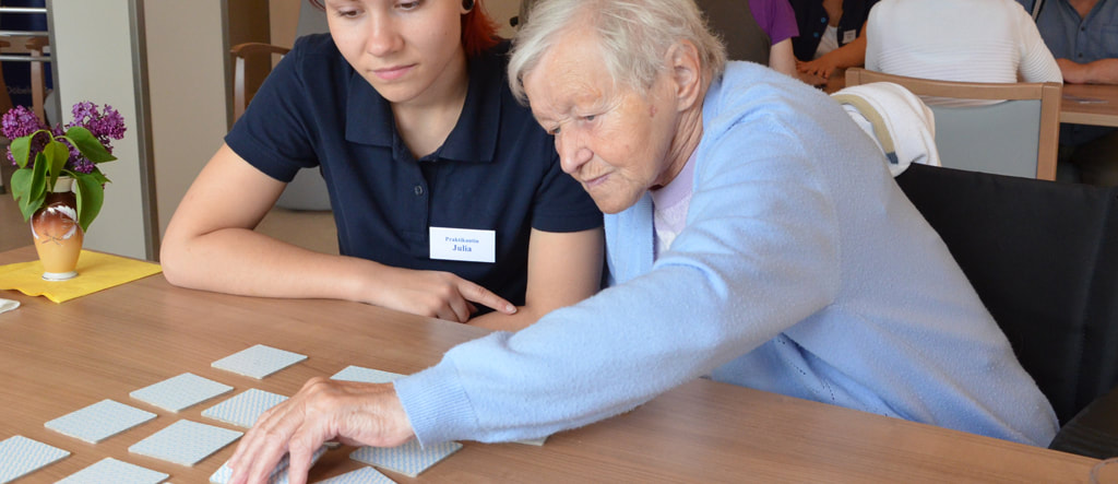 Seniorin spielt mit einer jungen Betreuerin Memory am Tisch