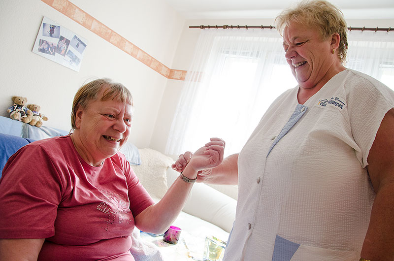 Pflegekraft und Klientin lachen gemeinsam im Wohnzimmer