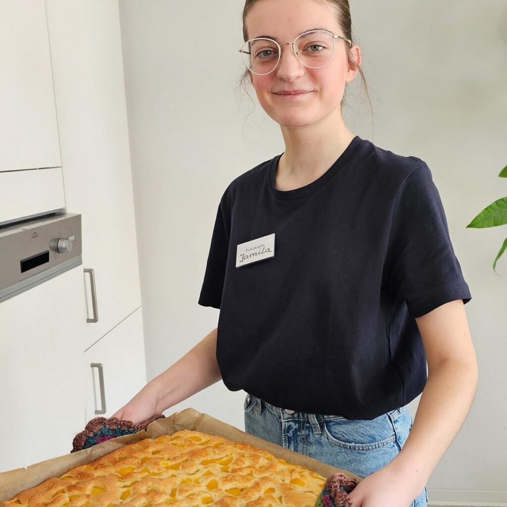 Junge Mitarbeiterin hält ein Blech mit frisch gebackenem Aprikosenkuchen