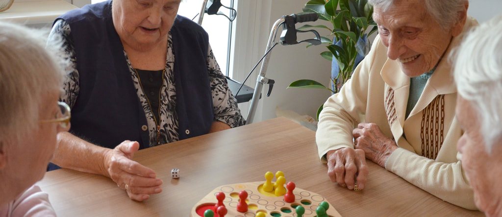 Gäste der Tagespflege spielen gemeinsam ein Brettspiel am Tisch