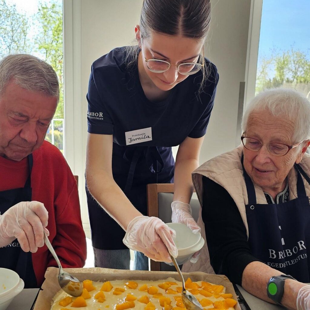 Pflegerin backt mit Gästen der Tagespflege einen Blechkuchen mit Aprikosen