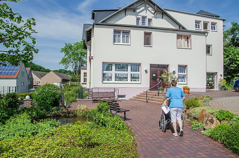 Garten vor der Villa „Zum Rüderpark“ in Roßwein, eine Pflegerin schiebt einen Rollstuhl über den Weg