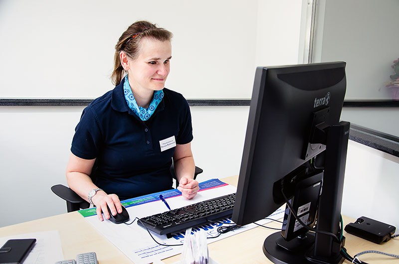 Mitarbeiterin in Brambor-Dienstkleidung arbeitet am Computer im Büro